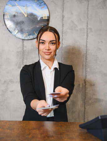 Young woman working at a reception desk, smiling and offering security key cards to a guest, providing hospitality serviceの写真素材