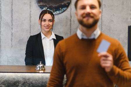 Happy man holding key card checking into hotel, smiling receptionist standing behind the front desk. Providing great hospitalityの写真素材