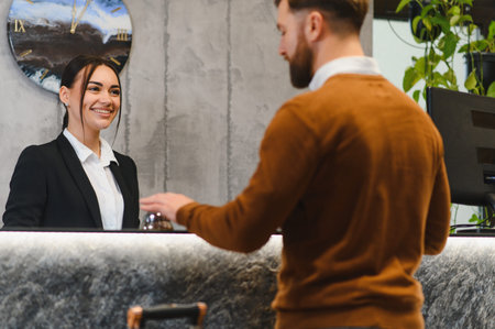 Smiling hotel clerk assisting a male guest arriving at the reception with luggage. Hospitality and customer service conceptの写真素材