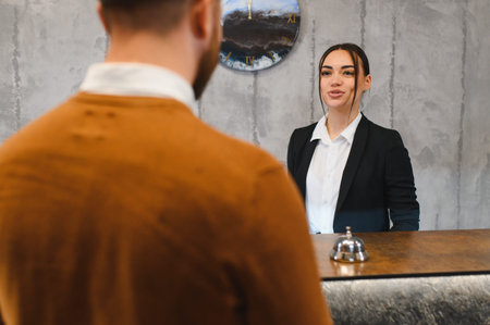 Female hotel receptionist smiling, welcoming male guest at the modern reception desk, offering quality customer serviceの写真素材