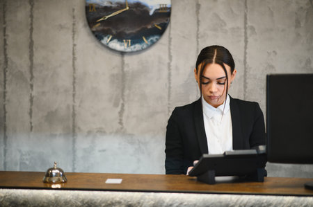 Female hotel concierge focused on work at the counter, providing hospitality service in a professional settingの写真素材