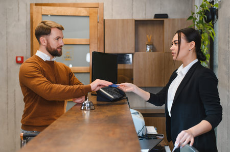 Man completing successful check in transaction, presenting credit card to a professional female receptionist at hotel counterの写真素材
