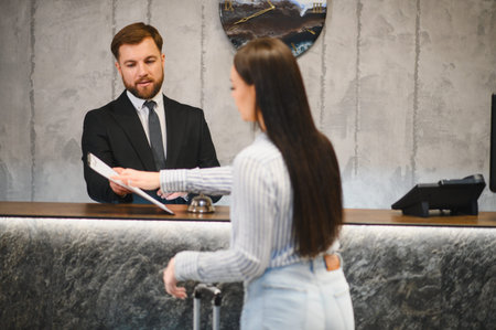Hotel receptionist helping a female guest with paperwork at the front desk, providing excellent customer service in the lobbyの写真素材