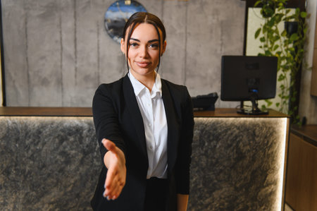 Friendly business woman welcoming with extended hand, demonstrating hospitality and partnership at modern reception deskの写真素材
