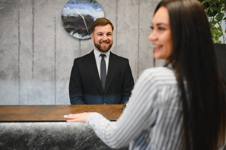 Friendly hotel receptionist greeting a female guest at the front desk, providing excellent hospitality and support for check inの写真素材