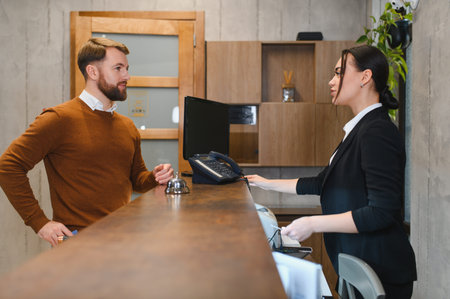 Male customer talking with female receptionist during check in at a modern hotel lobby, receiving hospitality serviceの写真素材