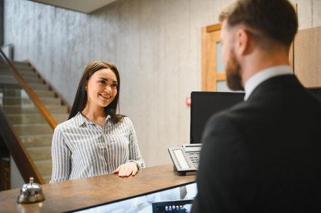 Smiling woman standing at a hotel reception desk, talking to a male receptionist, performing a check inの写真素材