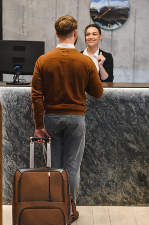 Traveler with luggage checking in at a contemporary hotel reception, a smiling female receptionist providing assistanceの写真素材