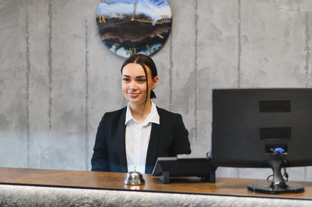 Young woman working as a concierge, providing guest service with a confident smile at a hotel reception counterの写真素材