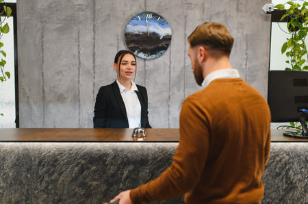 Hotel receptionist providing service to a male guest at the reception desk, focusing on hospitality and customer service interactionの写真素材