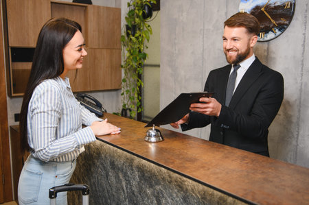 Smiling woman completing paperwork with a helpful receptionist for hotel check in, highlighting hospitality service and travelの写真素材