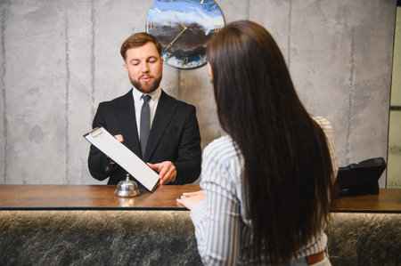 Hotel receptionist handing clipboard with documents to a female customer, providing friendly service at the reception deskの写真素材