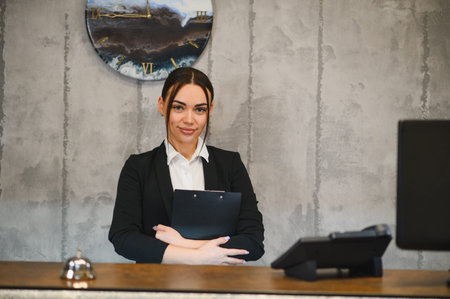 Young woman working as a front desk manager, standing and smiling at hotel reception. Providing professional customer serviceの写真素材