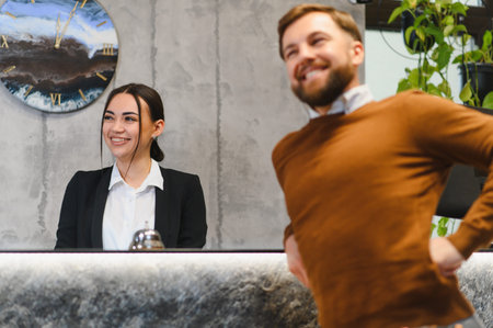 Friendly receptionist providing customer service, checking in a good mood guest experiencing back pain at modern hotel receptionの写真素材