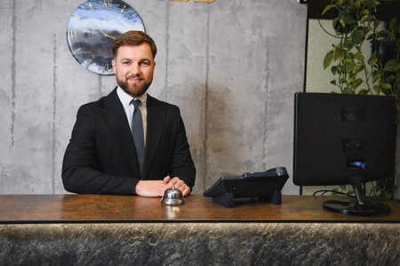 Smiling professional man standing behind a reception desk, providing friendly service, ready to assist guests. Modern hospitality conceptの写真素材