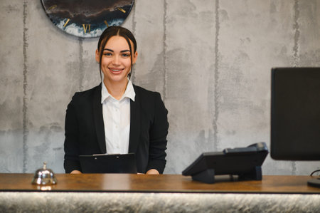 Young woman receptionist wearing a suit and smiling, standing at front desk, providing excellent customer serviceの写真素材