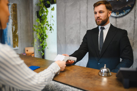 Receptionist holding a payment terminal for guest using a credit card. Focus on efficient hospitality service and customer interactionの写真素材