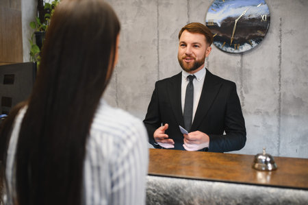 Friendly hotel receptionist at the front desk talking to a female guest. Providing excellent customer service and hospitalityの写真素材