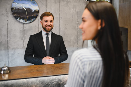 Smiling professional hotel receptionist greeting and helping a young female guest at a modern hotel lobby reception deskの写真素材