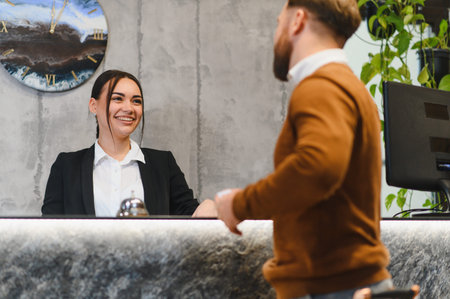 Friendly receptionist providing excellent customer service to a male guest checking into a hotel, offering hospitality and welcomeの写真素材