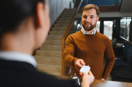 Bearded man handing a white card to a hotel receptionist for swift and efficient check in, highlighting hospitality and traveler serviceの写真素材