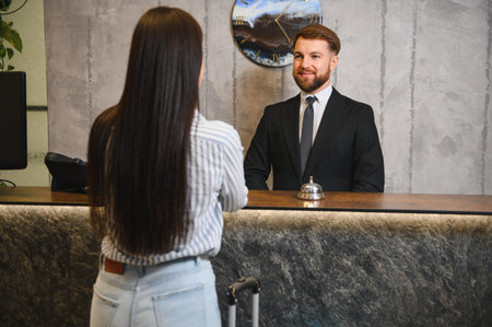 Male hotel receptionist providing service to a female guest at the reception desk, focusing on hospitality and customer careの写真素材