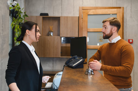 Hotel employee providing customer service to a guest, discussing check in procedures at the reception counterの写真素材