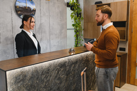 Man checking in at hotel reception, woman receptionist providing service and hospitality in modern lobbyの写真素材
