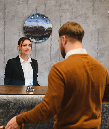 Young man checks in at hotel reception, smiling female clerk assists him at the front desk in a modern lobby settingの写真素材