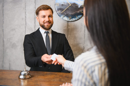 Friendly hotel receptionist assisting a female guest, offering a key card during check in at the reception deskの写真素材