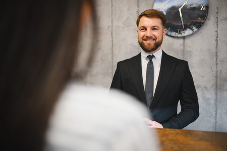 Friendly receptionist smiling, providing excellent hospitality and service to a client at the hotel front deskの写真素材