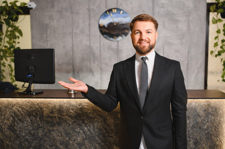 Smiling man in a suit working as a receptionist, presenting a welcoming gesture against a hotel...
