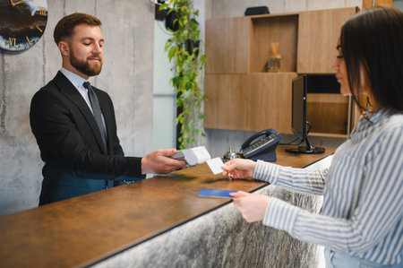 Hotel receptionist assisting a woman guest with check in, providing her with a key card and passportの写真素材