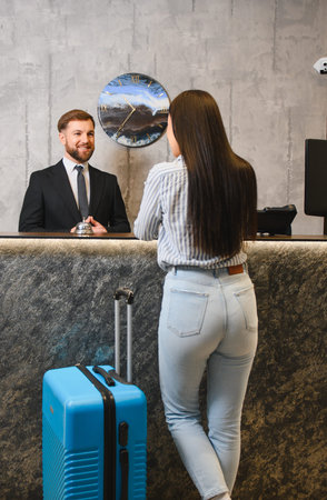 Friendly concierge assisting a woman with her luggage at the hotel reception desk, providing excellent hospitality serviceの写真素材