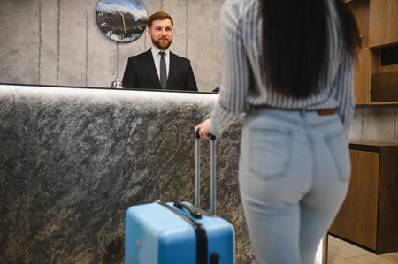 Traveler with luggage arriving at modern hotel reception for check in. Male receptionist greeting female guestの写真素材