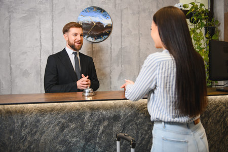 Friendly hotel concierge assisting a female traveler with her luggage at the reception desk in a contemporary lobbyの写真素材