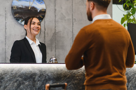 Friendly hospitality worker talking to client at hotel reception desk, providing quality service in a modern lobbyの写真素材
