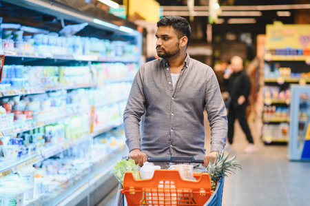 Customer pushing a shopping cart filled with fresh food items, browsing refrigerated shelves in a modern grocery storeの写真素材