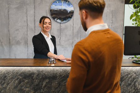 Friendly hotel receptionist handing over key card to a male guest at the modern check in counter, providing excellent serviceの写真素材