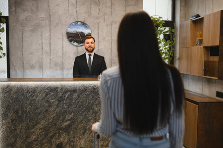 Smiling male receptionist interacting with female business traveler checking into modern hotel lobby, providing professional service and hospitalityの写真素材