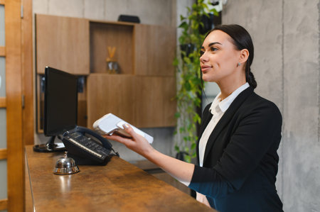 Smiling receptionist holding payment terminal for customer transaction at a modern hotel front desk, providing hospitality serviceの写真素材