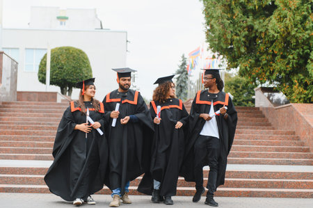 Happy multi ethnic graduates walking outside university building, celebrating academic achievement and a bright futureの写真素材
