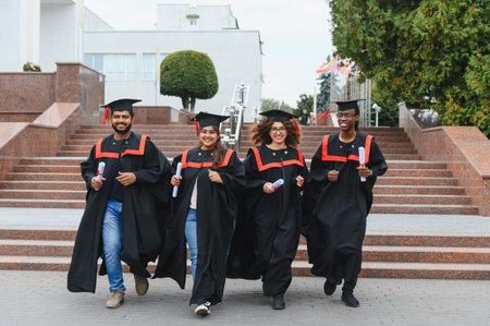 Group of happy diverse university graduates walking outdoors, celebrating academic achievement and holding their diplomasの写真素材