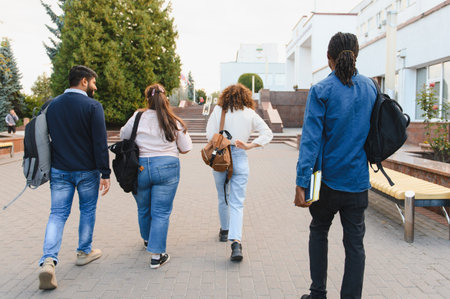 Group of diverse university students with backpacks walking on campus, heading towards a building for their classes and studiesの写真素材