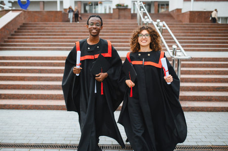 Diverse students in graduation gowns and caps smiling, holding diplomas after completing university education, representing achievementの写真素材