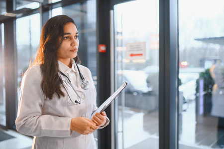 Young Indian female doctor in medical uniform standing in a modern clinic or hospital, holding a clipboardの写真素材
