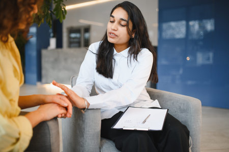 Indian psychologist providing support and empathy to a woman client during a mental health therapy session in a modern officeの写真素材