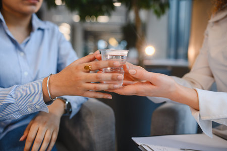 Professional psychologist providing water to a distressed Indian female patient during a therapy session, offering support and careの写真素材