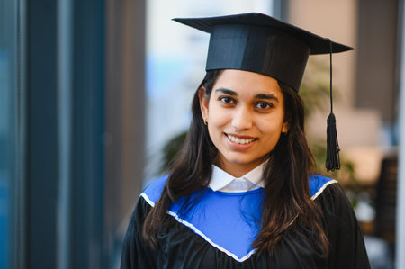 Young Indian woman wearing graduation cap and gown, smiling at the camera, celebrating her educational achievement and futureの写真素材
