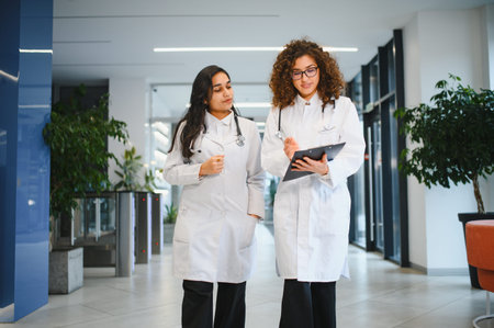 Diverse medical professionals wearing white coats, stethoscopes, and discussing patient charts while walking in a modern clinicの写真素材